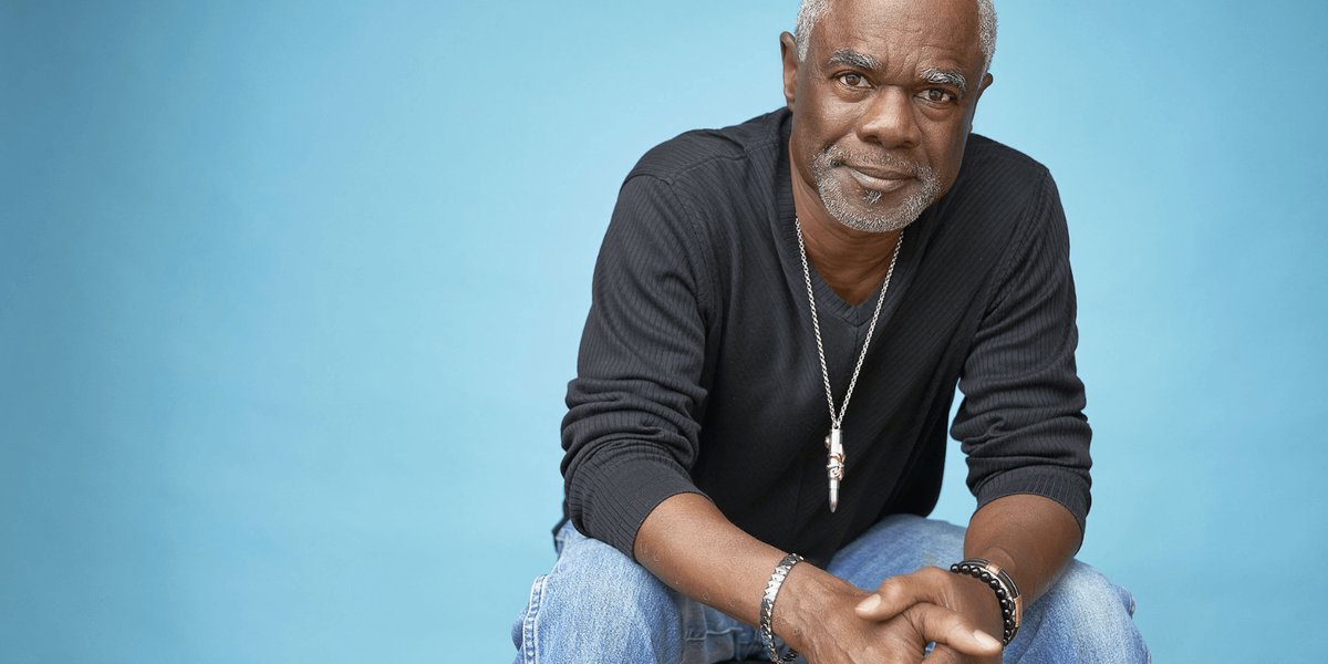 Actor Glynn Turman sitting on a stool in front of a blue background