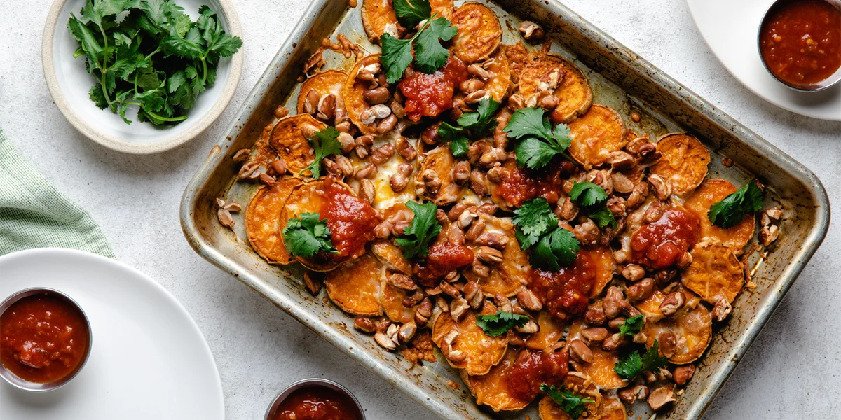 Sweet potato nachos on a sheet pan next to plates of fresh cilantro and salsa.