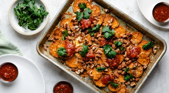 Sweet potato nachos on a sheet pan next to plates of fresh cilantro and salsa.