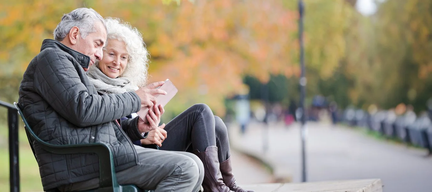 Pareja sentada en un banco del parque utilizando una tableta digital.
