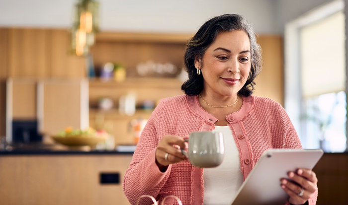A Clover member reading on a tablet with a cup of coffee in her kitchen