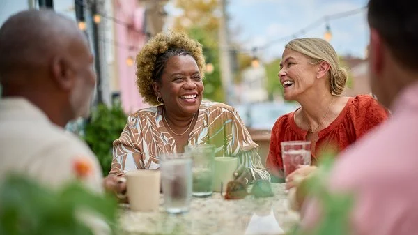 A group of people laugh at a dining table.