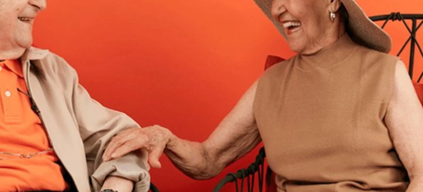 Couple sitting in chairs laughing against an orange background