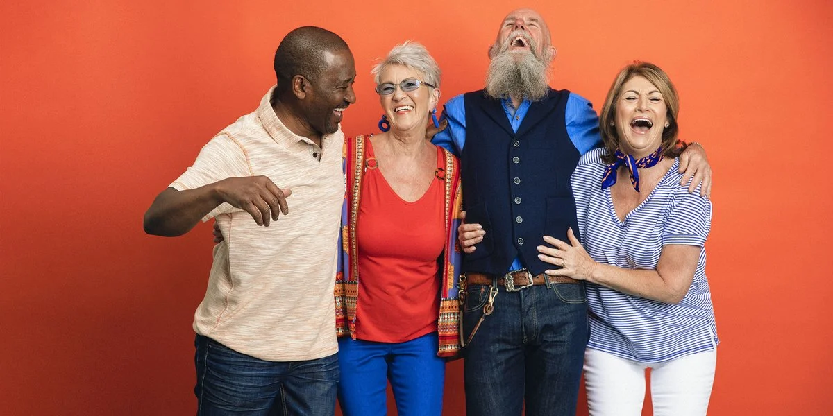 Group of 4 friends laughing with each other in front of an orange wall