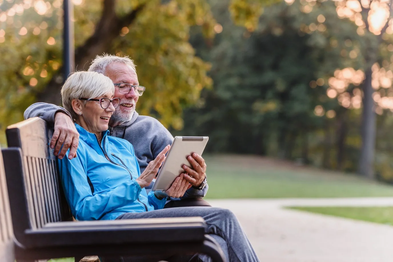 Couple sitting on a park bench using a digital tablet.