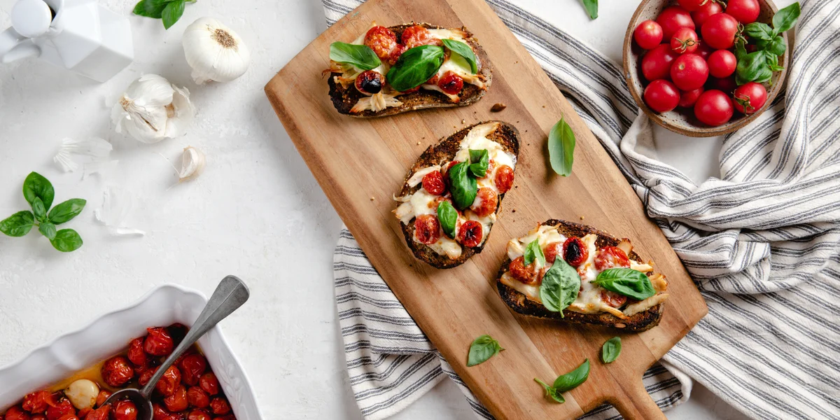 Chicken melt garnished with basil and tomatoes placed on a wooden slate.