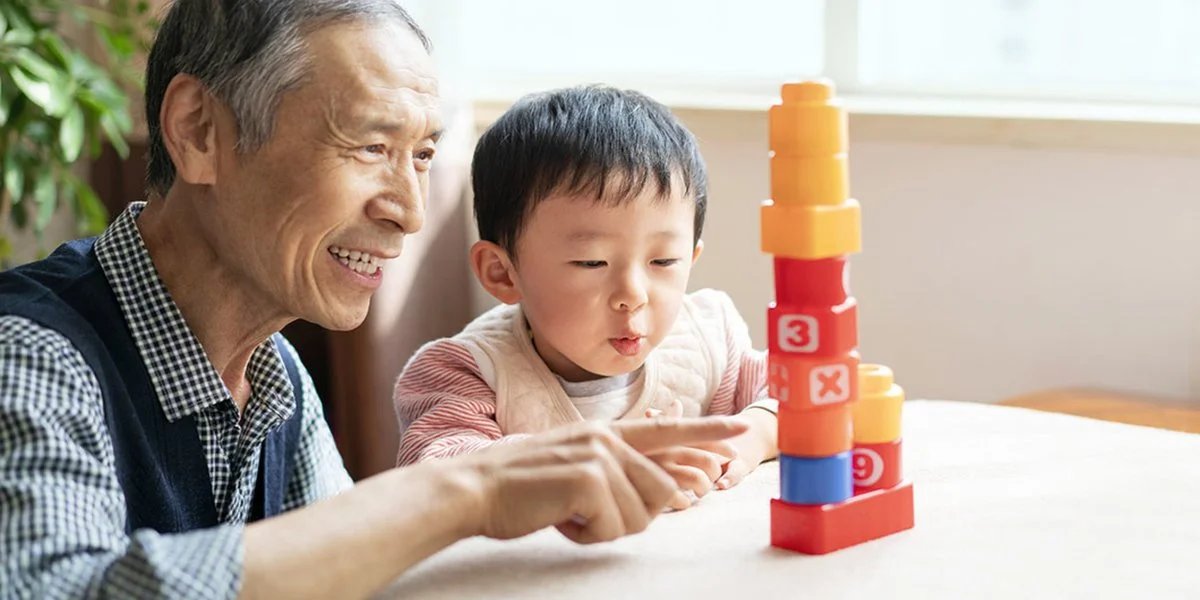 Grandfather and grandchild sitting at a table and playing with blocks