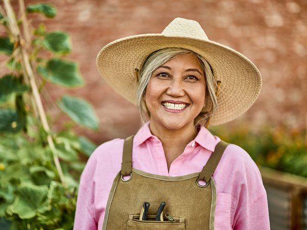 A smiling Clover member gardening in a straw hat and work apron