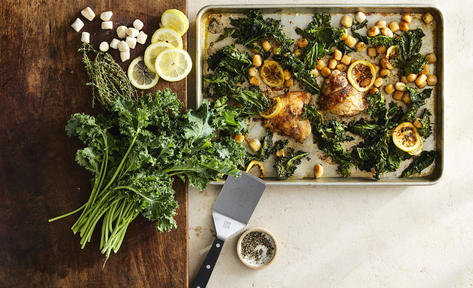 Fresh kale, gnocchi and lemon chicken thighs plated on a table with a spatula