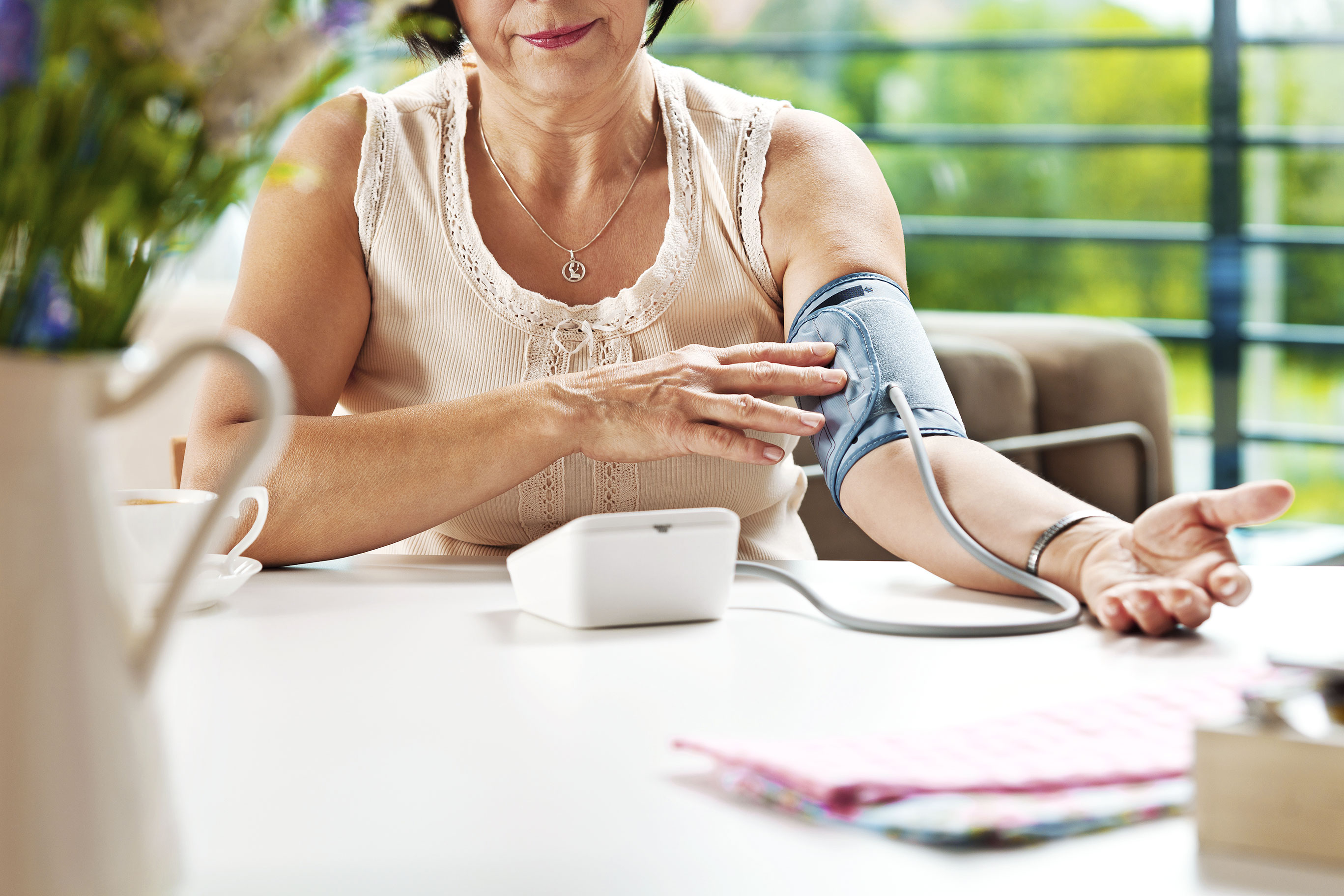 Woman sitting at a table using a blood pressure reader to measure her own blood pressure