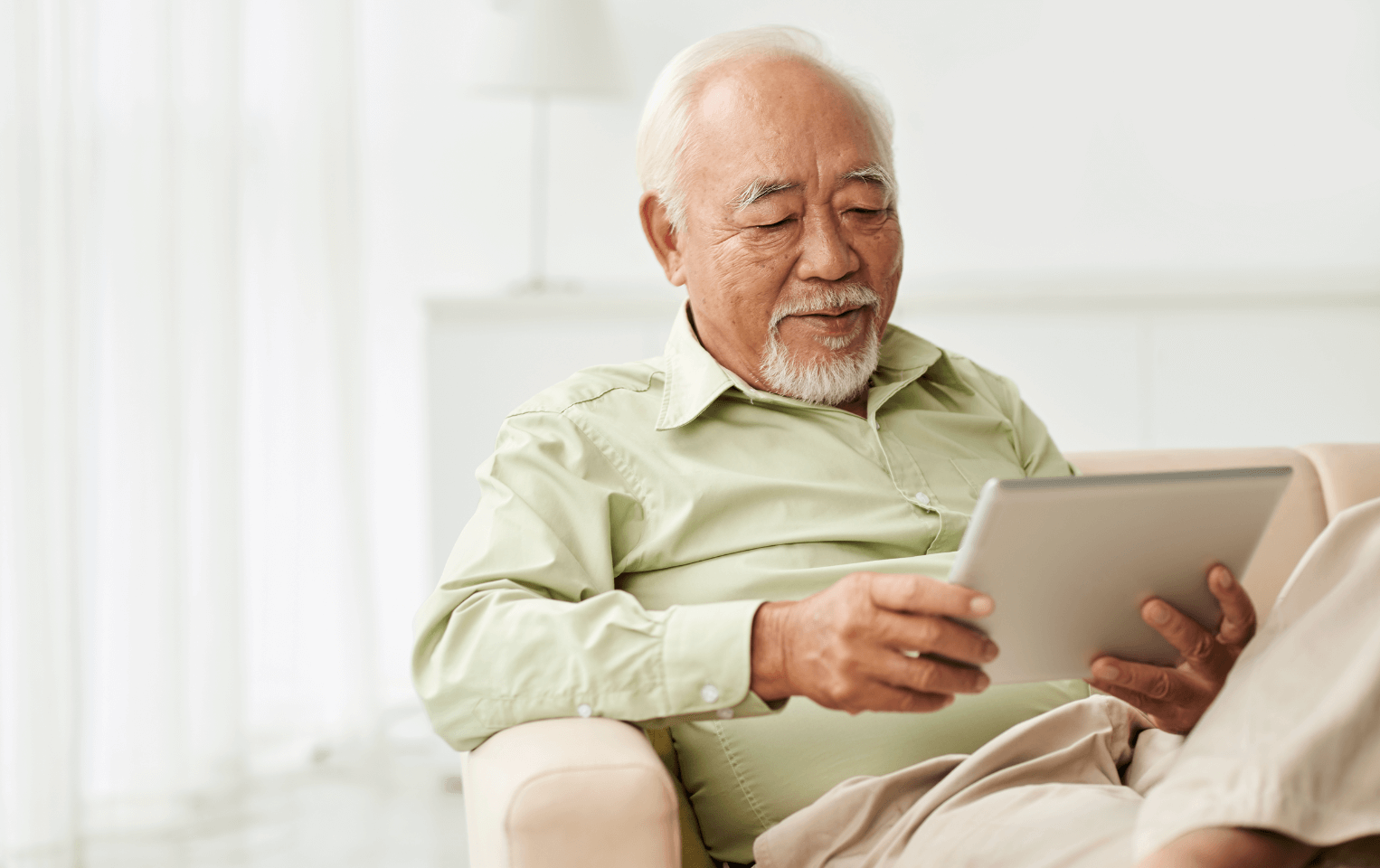 Elderly man sitting on a couch with his tablet device.