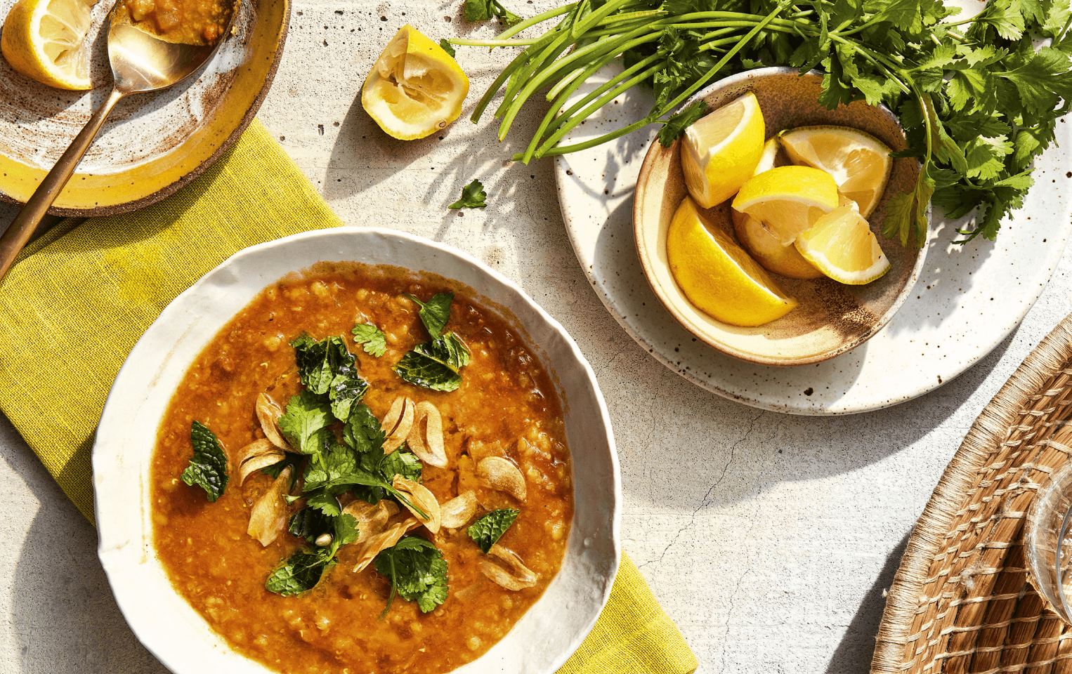 bowl of red lentil dal with lemons and herbs on a table