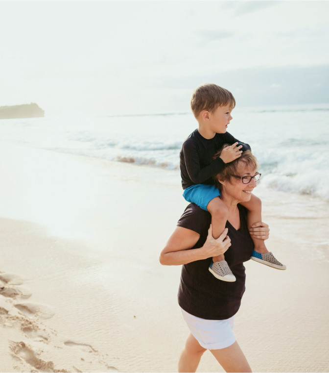 Grandmother carrying her grandson on her shoulders walking along the beach