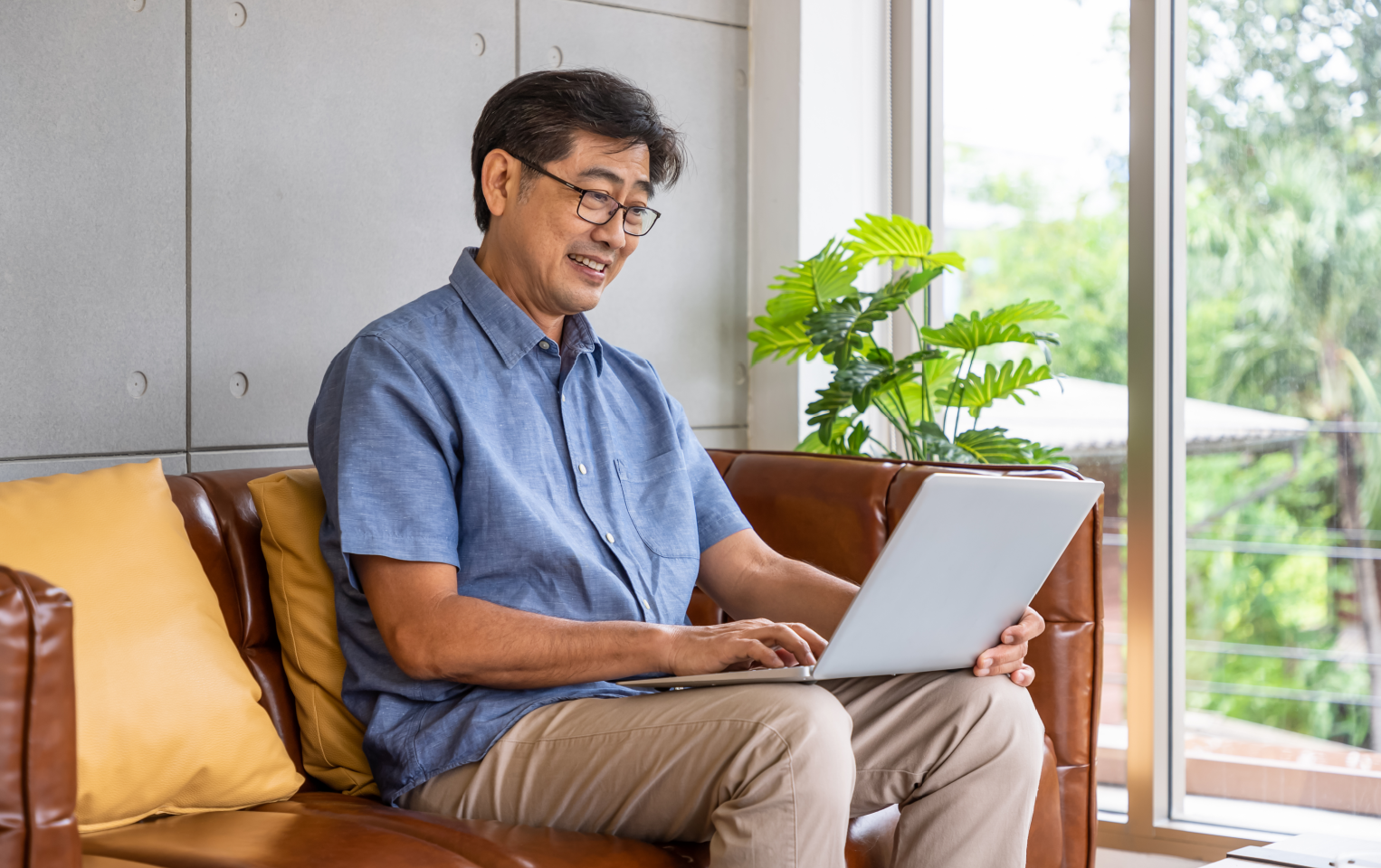 A man in a blue shirt on his computer while sitting on a brown couch