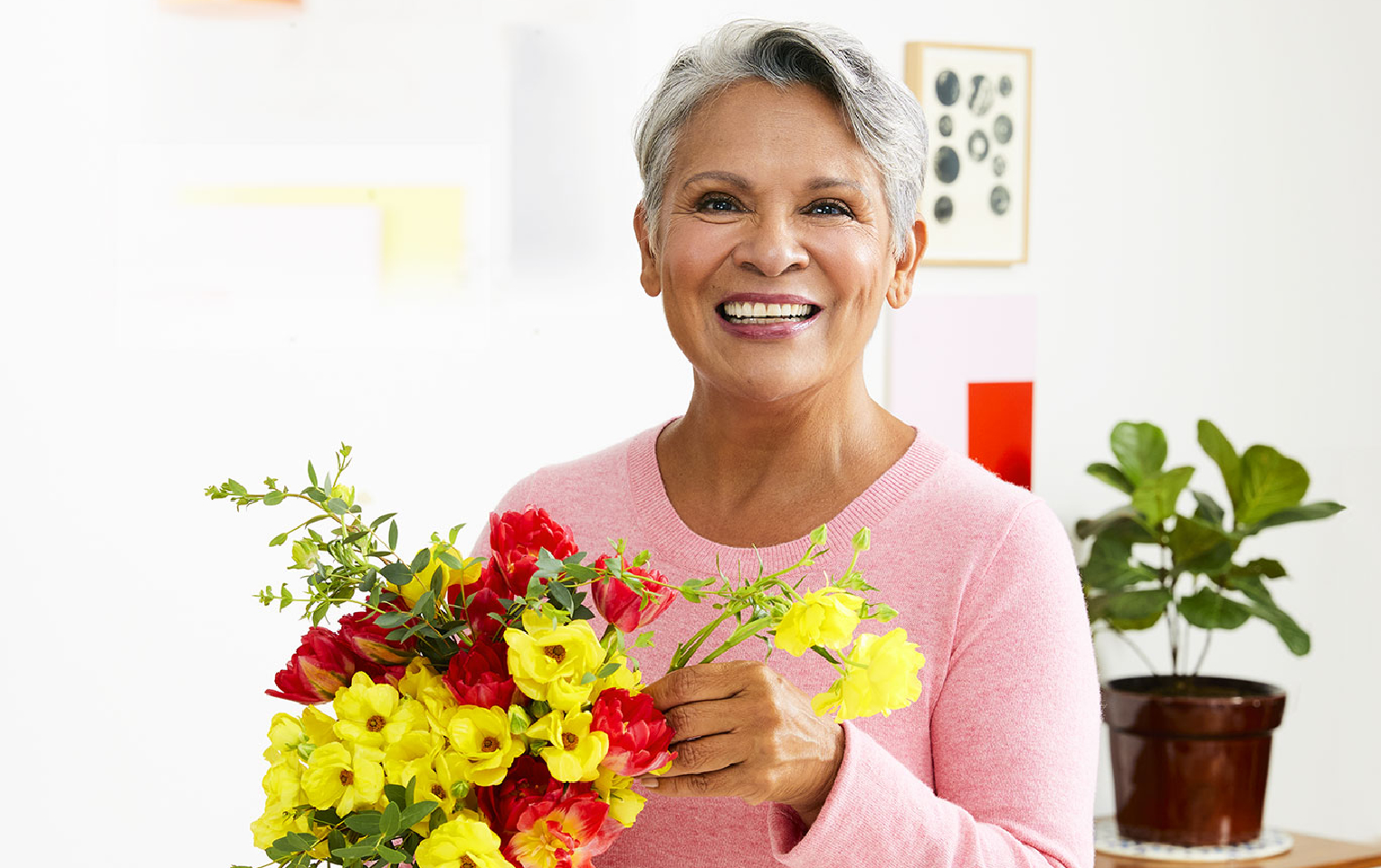 woman in a pink sweater arranging a bouquet of yellow, red, and pink flowers on the countertop in the kitchen