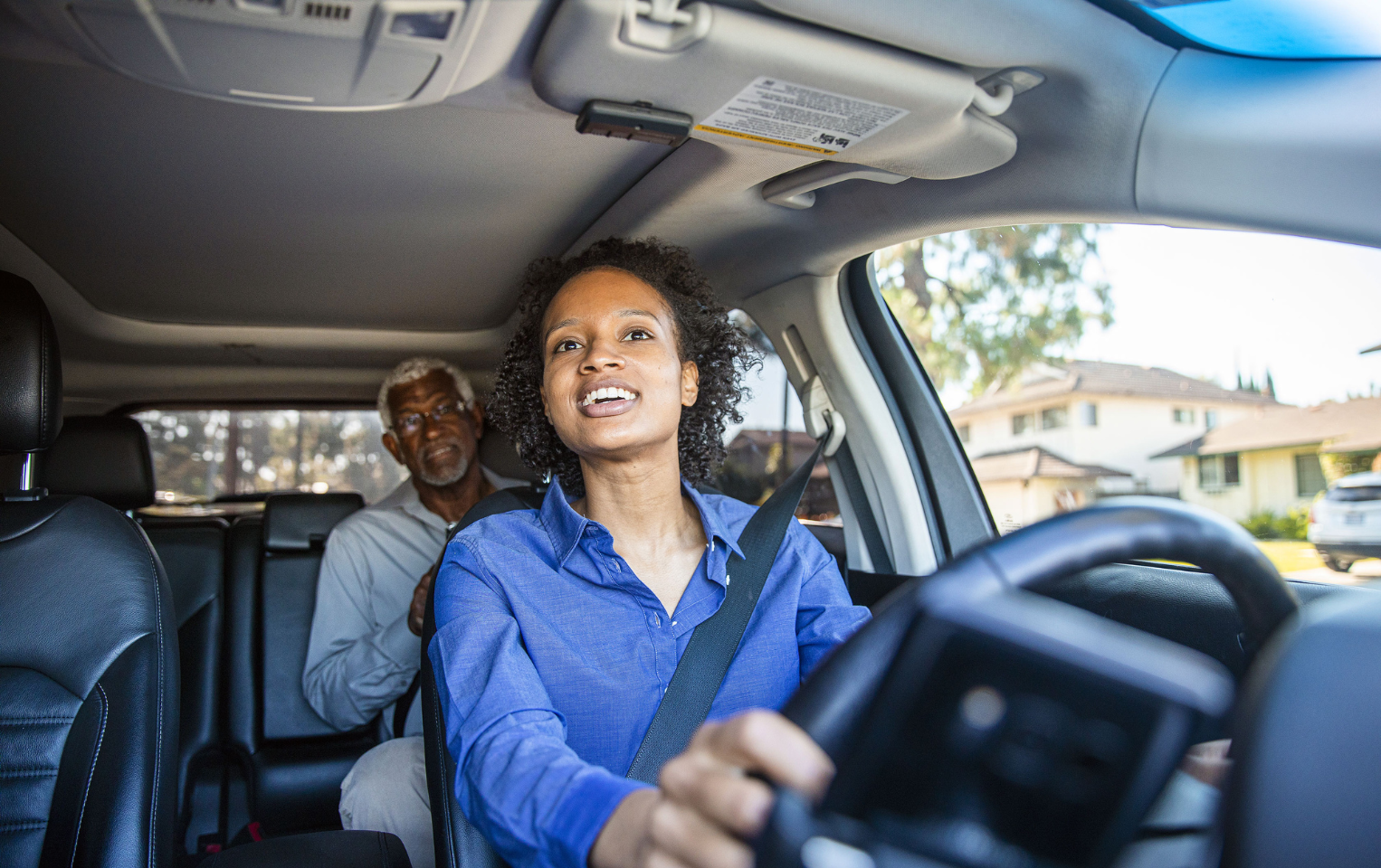 Young woman in a car driving with an elderly man in the back seat.