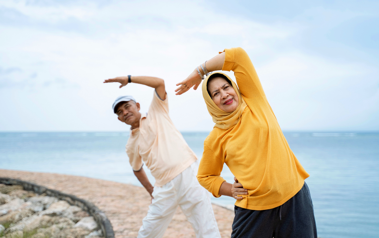 Woman in a yellow shirt and yellow headscarf with a man in a white polo stretching by the water