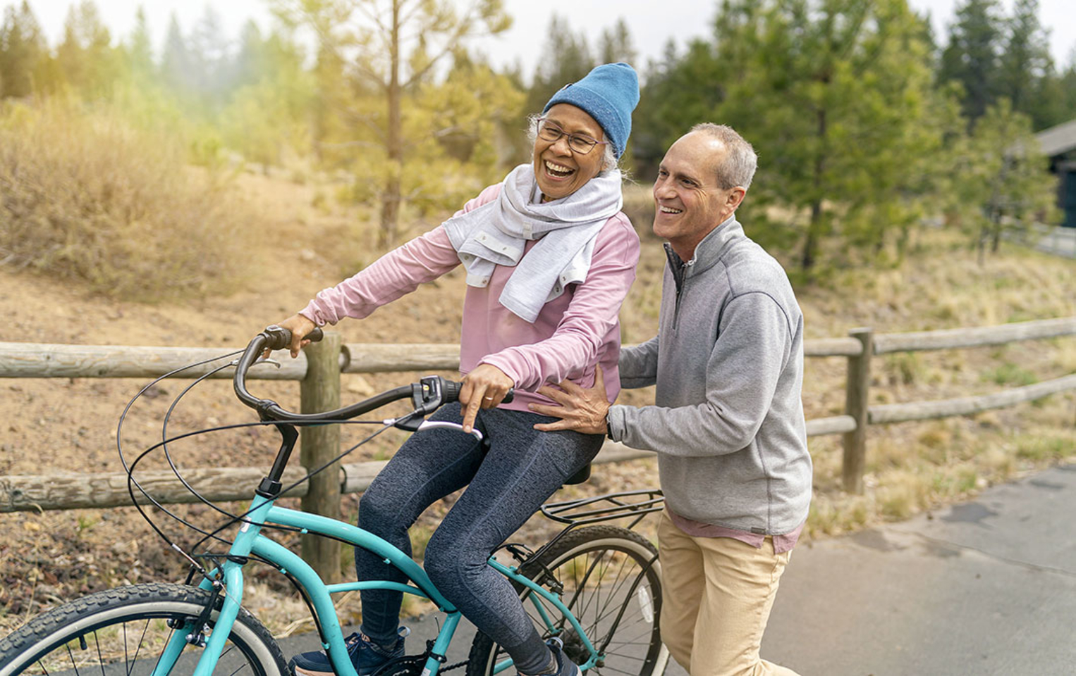 Woman on a blue bicycle with a man helping her learn how to ride the bicycle