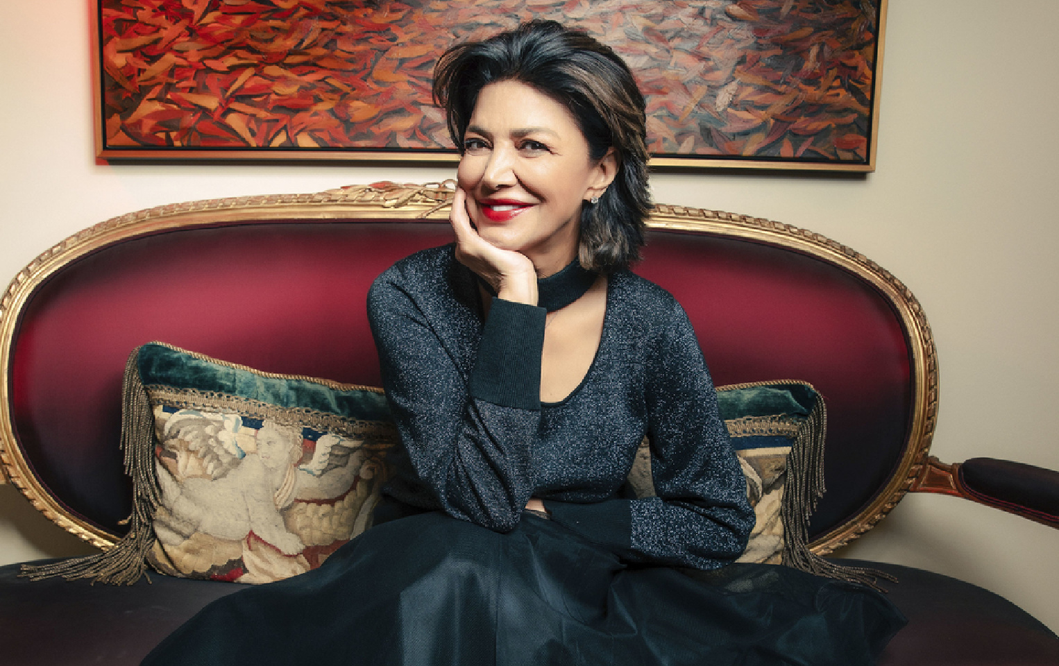 Actress Shohreh Aghdashloo in a formal dress sitting on a red loveseat