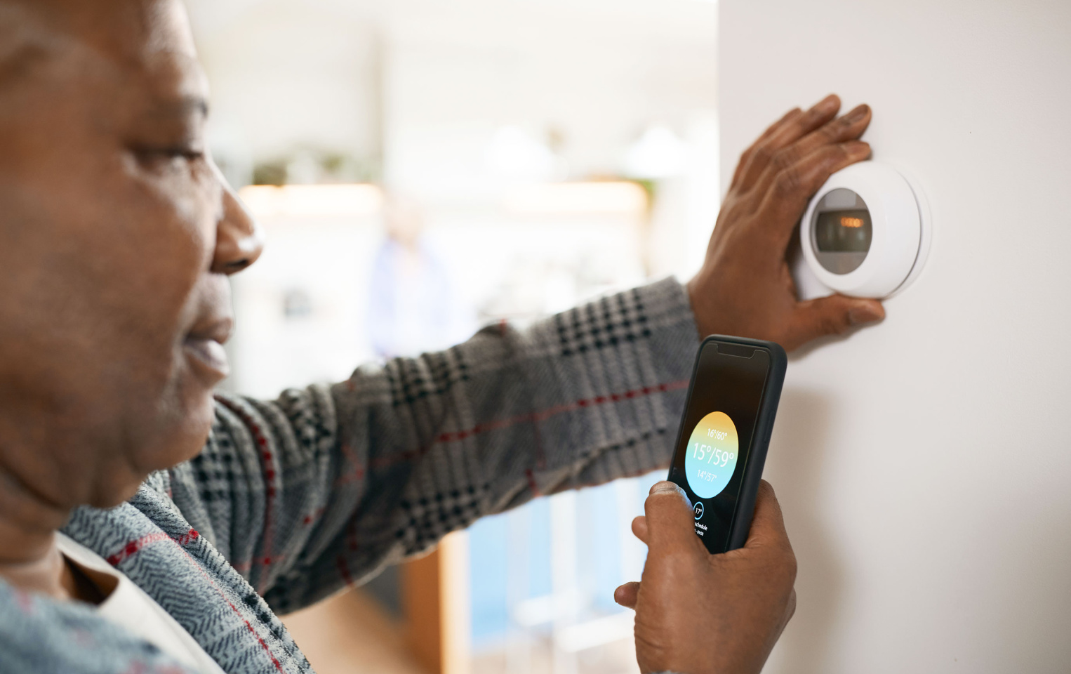 Woman standing in front of her smart thermostat while using her phone to adjust the temperature