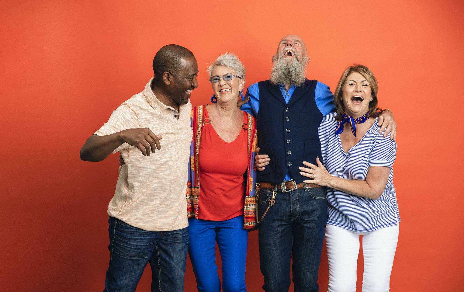 Group of 4 friends laughing with each other in front of an orange wall