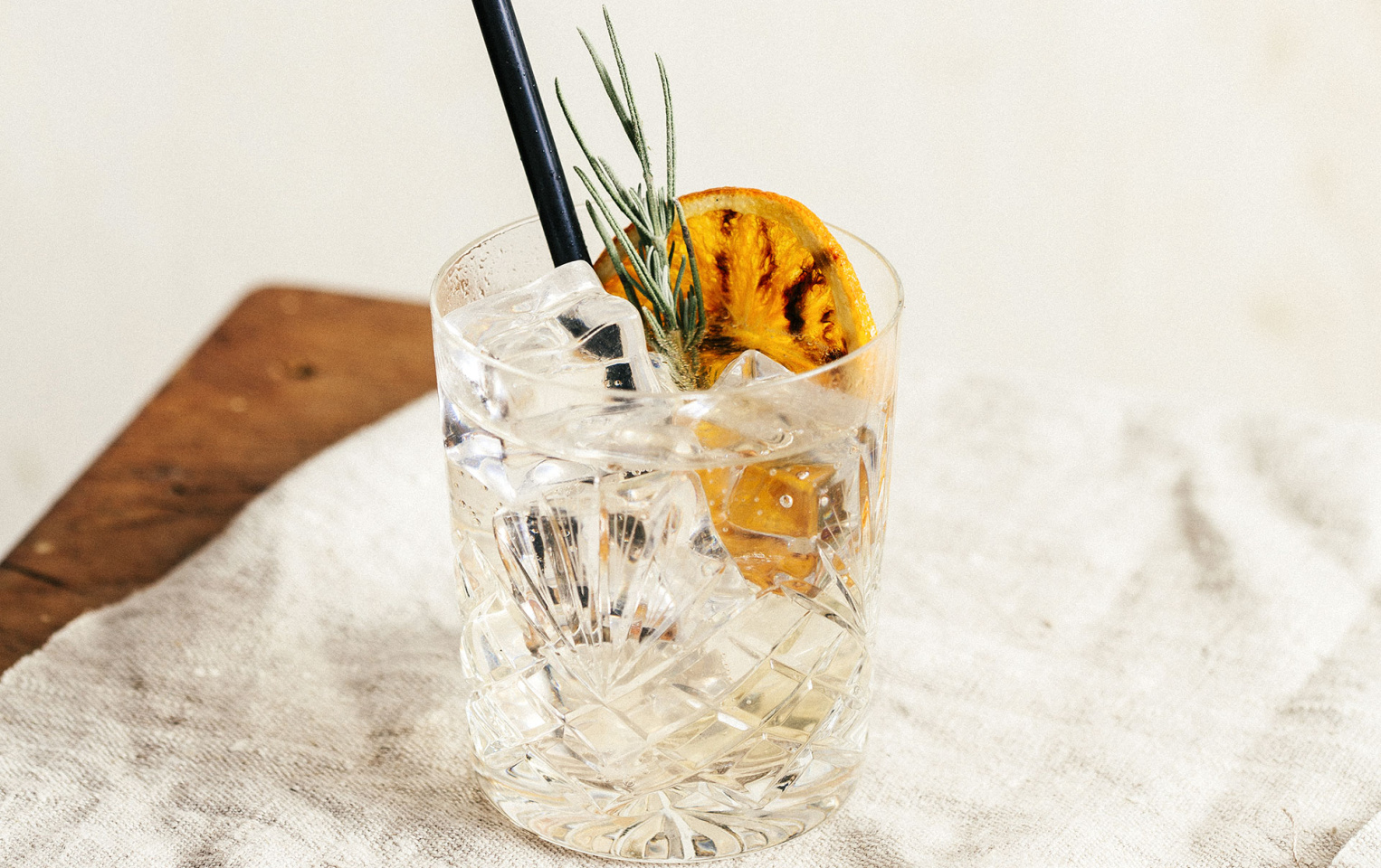 Glass of orange tonic with a sprig of rosemary and burnt orange garnish placed on a white table cloth