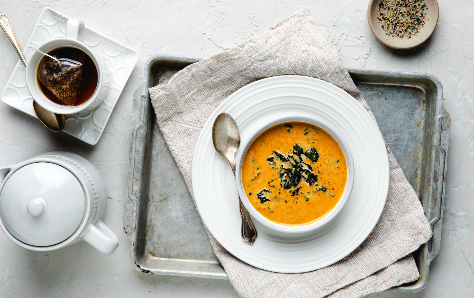 A bowl of sweet potato soup on a concrete table with a teapot and tea cup next to it.