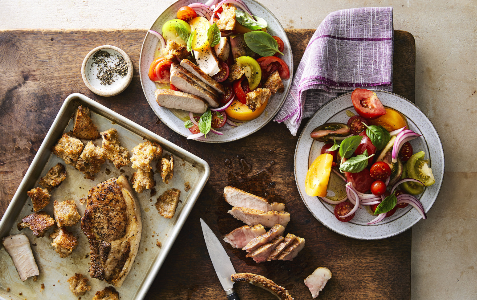 Roasted pork chops with marinated tomatoes and croutons plated on a table with a napkin