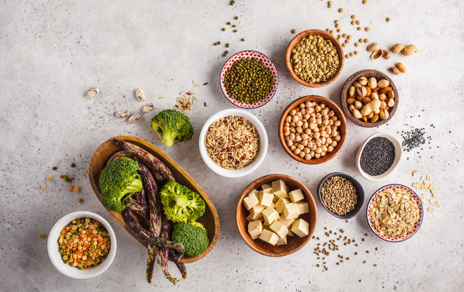 A variety of brown bowls filled with vegetables, tofu, and chickpeas on a grey table.