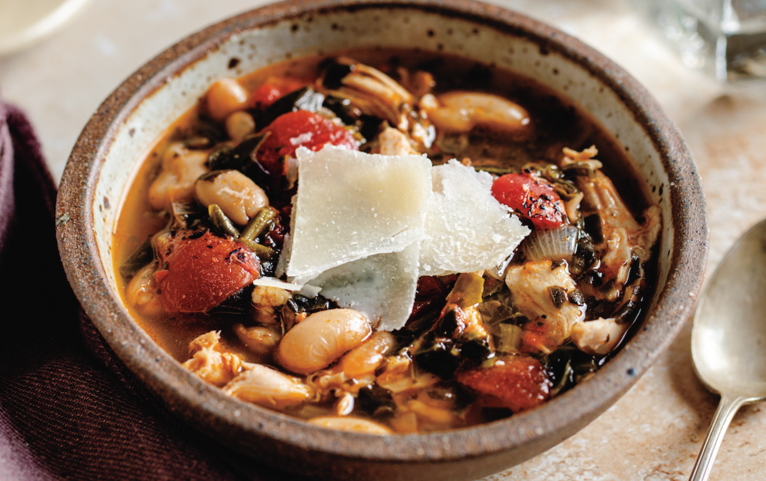 Tomato, Spinach, Cannellini Bean, and Chicken Soup in a bowl with a spoon laying next to it.