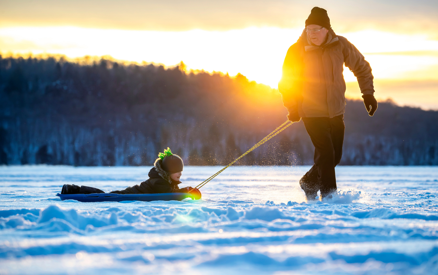 Grandfather pulling grandson on a sled on a snowy day.