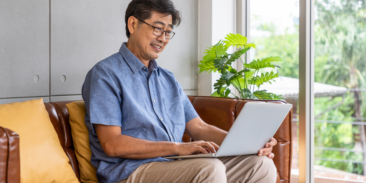 A man in a blue shirt on his computer while sitting on a brown couch