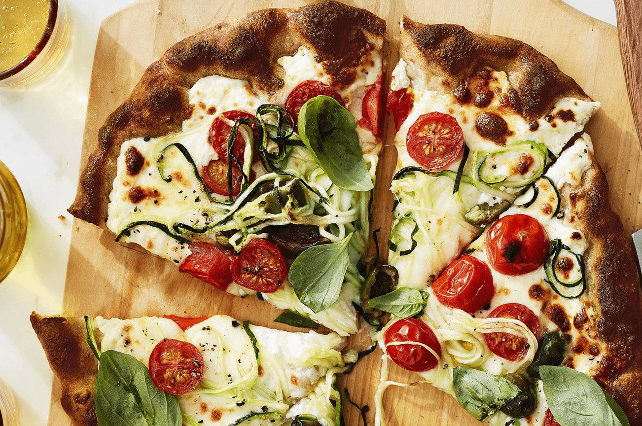 pizza with tomatoes, zucchini spirals and basil on a cutting board